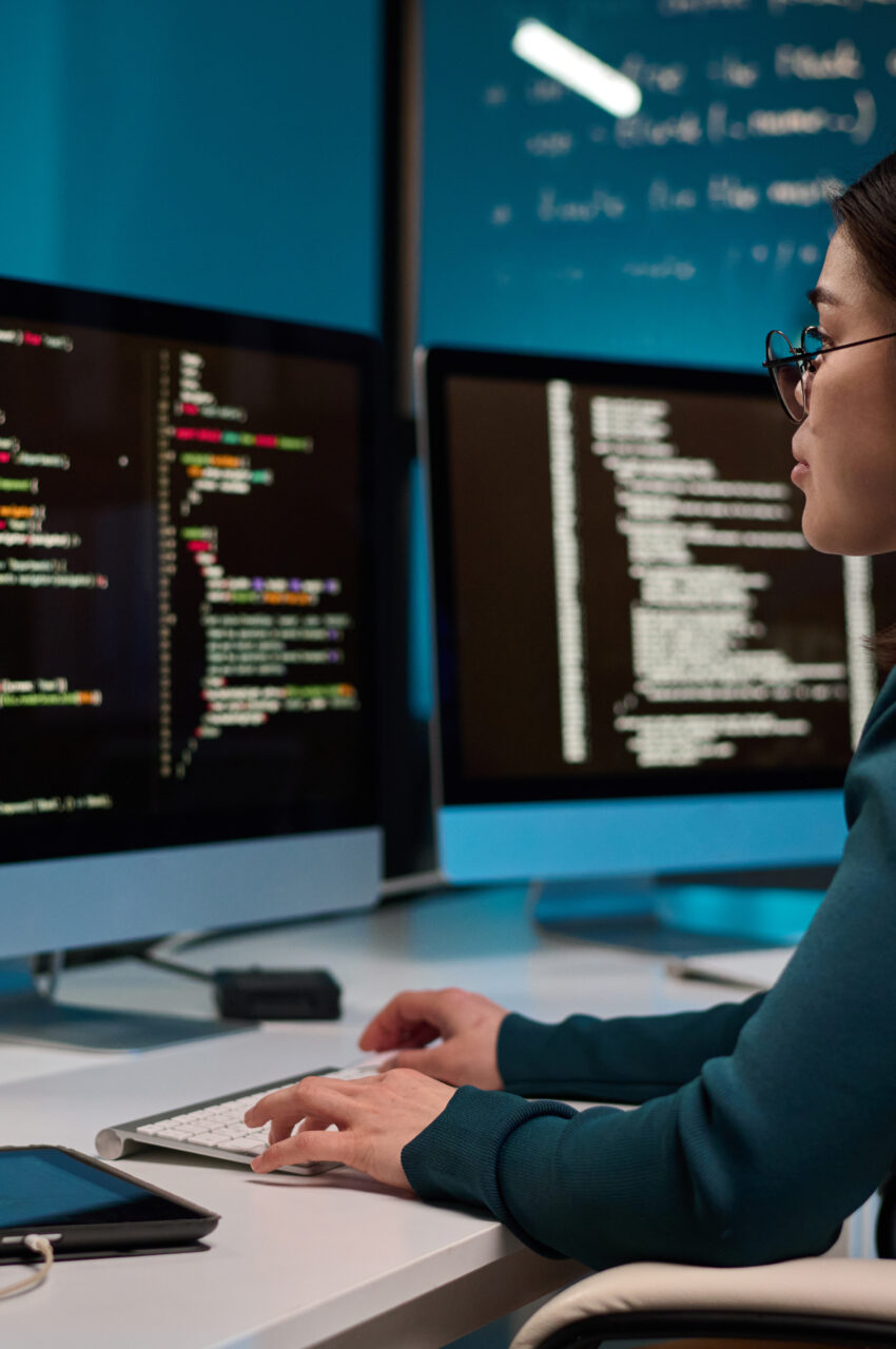 Portrait of young woman as software developer writing code while using computer at office workplace in blue light copy space